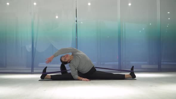 Young Woman Doing Stretching Using Fitness Gum and Tilts the Body in Different Sides on Mat in the