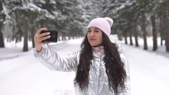 Girl Makes Selfie Using Smartphone While Standing in a Winter Forest
