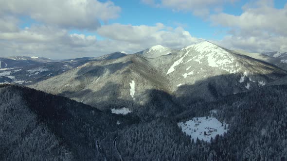 Aerial winter landscape with small rural houses between snow covered forest in cold mountains.