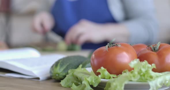 Close-up of Fresh Organic Vegetables Lying on the Table As Blurred Female Hands Cutting Cucumber at