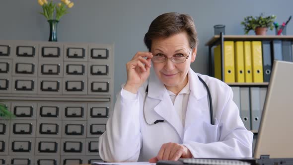 Portrait of a Senior Positive Female Doctor 50s Sitting in Her Office with a Laptop