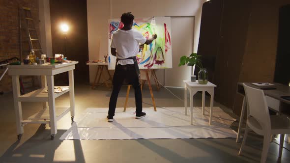 African american male artist wearing apron painting with paint brush on canvas at art studio