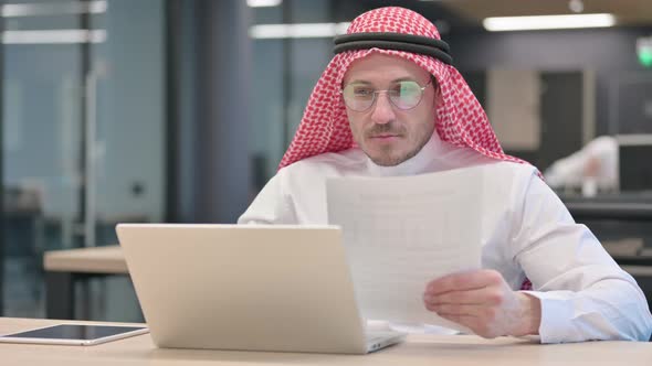 Middle Aged Arab Man with Laptop Celebrating Success on Documents