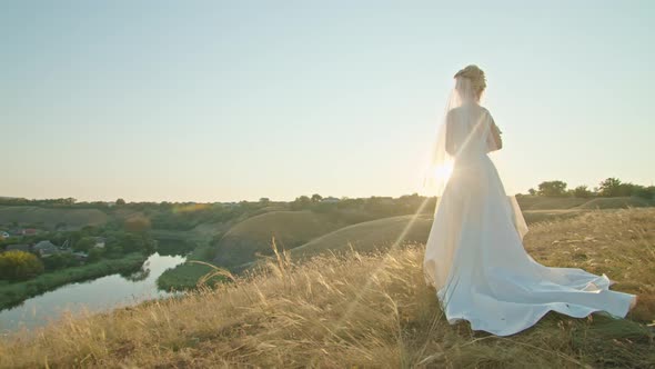 Happy Young Woman Bride at Sunset Standing on a Mountain Hill Enjoying a Pleasant View of the River