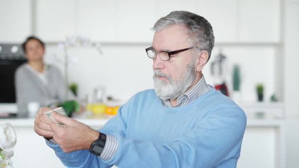 Portrait of Senior Man in Eyeglasses Examining Dollar Banknote Indoors