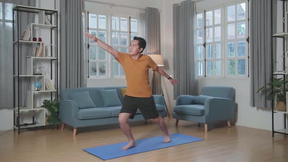 Asian Man Doing Yoga In Warrior Ii Pose On Mat  At Home