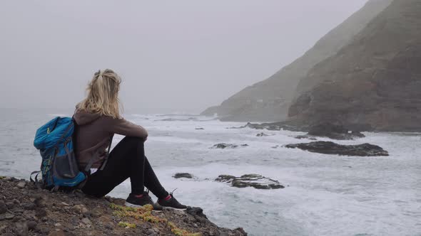 Tourist Female Admiring Powerful Waves Splashing Into Rocky Coastline. Huge Volcanic Mountains