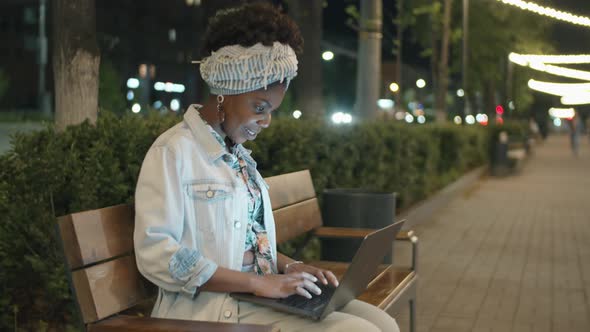 Afro Woman Sitting in Park in Evening and Using Laptop