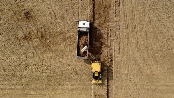 Yellow excavator digs the ground and loads it on a truck. Top view.