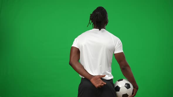 Back View Concentrated Confident African American Football Player with Ball Standing at Green Screen