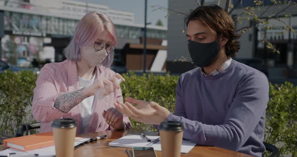 Students Wearing Masks Studying in Street Cafe Spraying Hands with Sanitizer