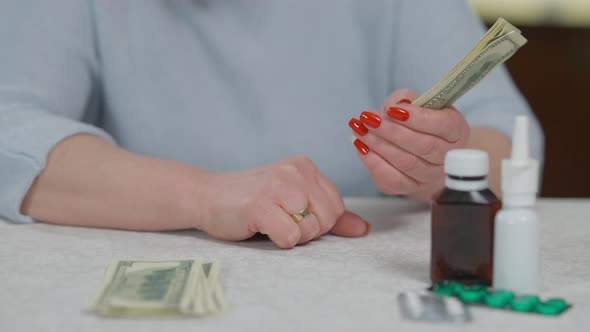 Female Senior Hands Counting Cash Money with Medications Pills on Table