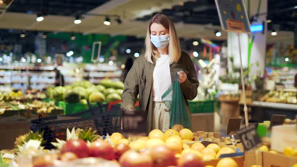 Young woman in face medical protective mask chooses and picks in eco bag vegetables or fruits 