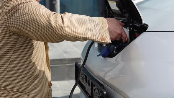 Unrecognizable Senior Man Plugging in Charging Cable to to Electric Vehicle