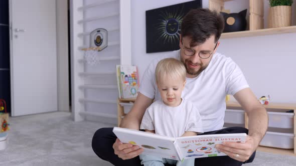 Father and Toddler Son Reading a Book and Having Fun at Home