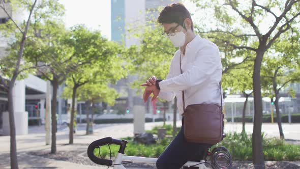 Asian man wearing face mask using smartwatch while sitting on his bicycle on the street