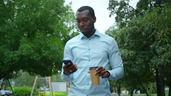 Portrait of Stylish Black African Man Walking Down the Street Using Smartphone for Social Media.