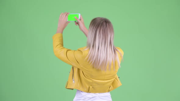 Rear View of Young Rebellious Blonde Woman Taking Picture with Phone