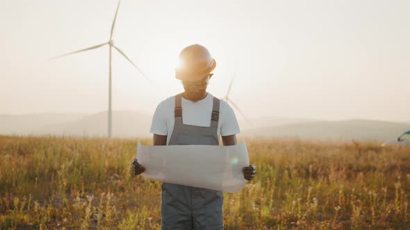 Focused African American Man with Blueprints in Hands Standing Among Farm with