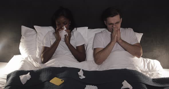 Sick Multi-ethnic Couple Blowing Nose Lying in the Bed. Feeling Unwell Concept.