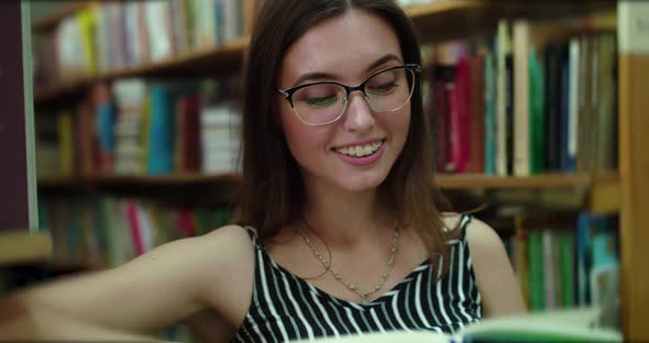 View of Happy Girl Overlooks a Book Fascinately in the Library