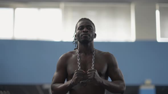 Portrait of Confident Serious African American Shirtless Man Posing in Gym with Chain on Neck