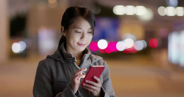 Woman use of mobile phone online in the city at night