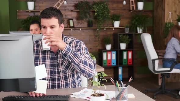 Confident Businessman Typing on His Computer and Enjoying a Cup of Coffee