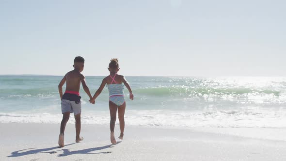 African american siblings running and wearing swimming suits on sunny beach