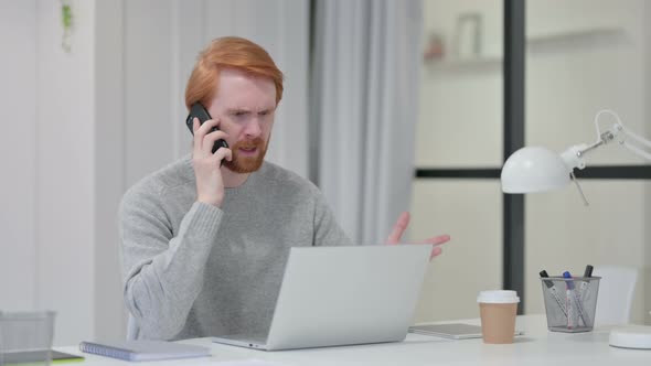 Angry Redhead Man with Laptop Talking on Smartphone 