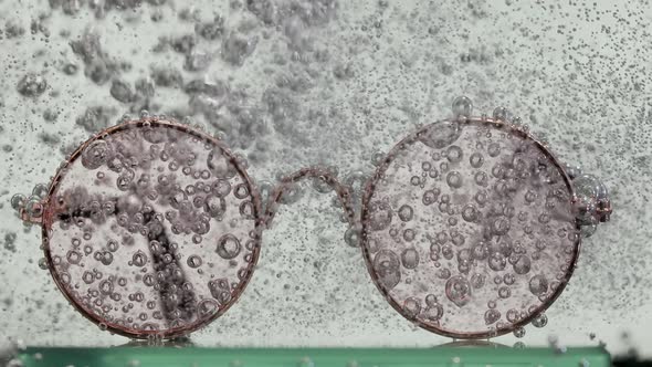 A Stream of Soda is Poured Onto Round Glasses in Water Causing a Vortex of Oxygen Bubbles