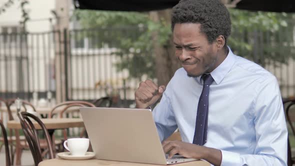 Yawning African Businessman Working on Laptop in Outdoor Cafe