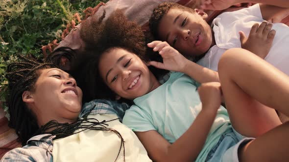 A smiling afro-american family mother and her children are having fun lay down on the plaid