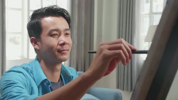 Asian Artist Man Holding Paintbrush And Mixing It With Colour Before Painting On The Canvas