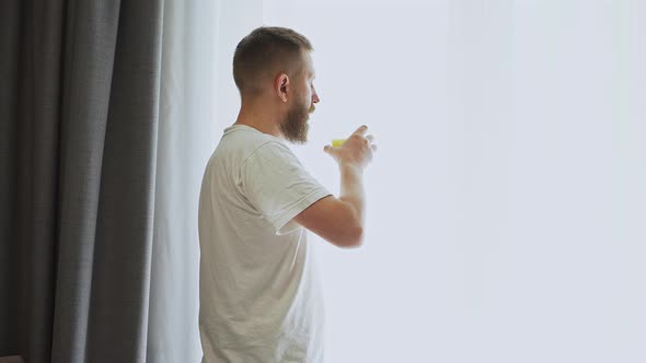 bearded man near the window drinking orange juice. fresh squeezed orange juice