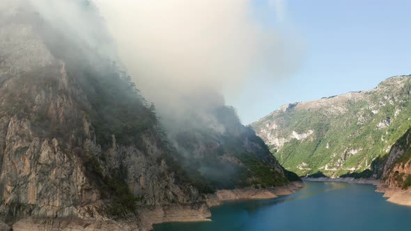 Cloud of white smoke lingering to the hillside, resembling fog or mist and covering blue sky