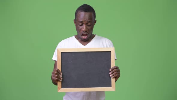 Young African Man Showing Blackboard and Looking Shocked