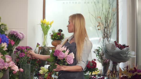 Side View of a Young Attractive Woman in Apron Working in Floral Shop and Arranging Bunch of Flower