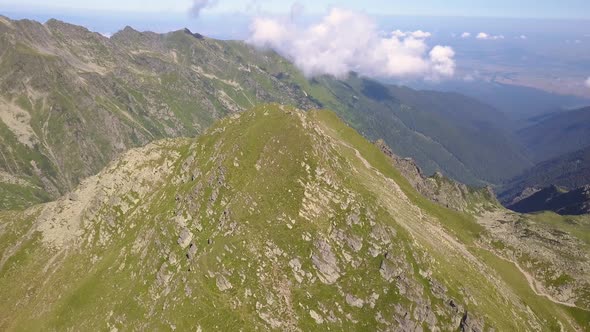 Hikers on distant peak looking out on dramatic landscape above the clouds. Aerial view from drone of