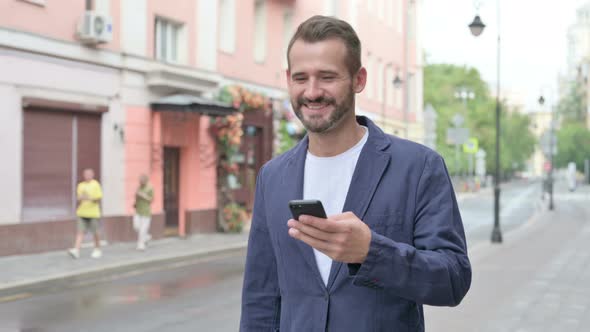 Man Using Phone While Walking on Beautiful Street