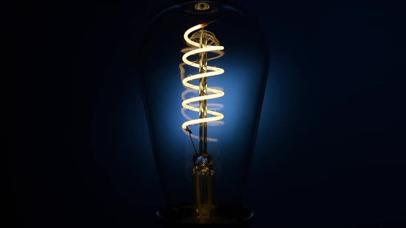 Electric Vintage Edison Light Bulb with a Spiral Flashing on a Blue Background