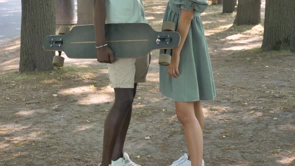 Black Man Carrying Skateboard Stands Talking to White Woman