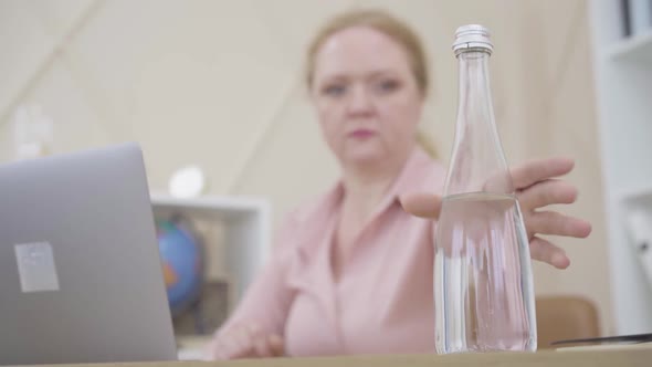 Blurred Caucasian Woman Taking Bottle of Water and Drinking. Busy Senior Businesswoman Feeling