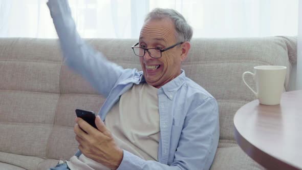 Elderly Man Rejoices Looking Into Smartphone