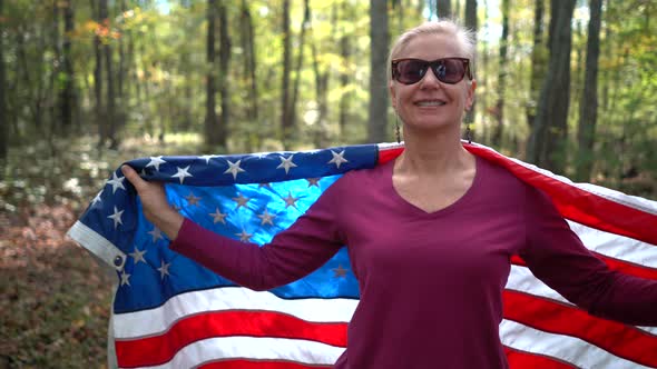 Pretty, blonde woman walking through a sunlit forest holding out a flag and then wrapping it around