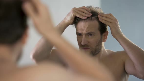 Middle-Aged Man Looking in Mirror at His Bald Patches, Hair Loss Problem