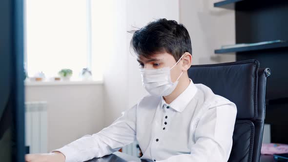 A Young Man in a Medical Mask Performs Homework at a Computer
