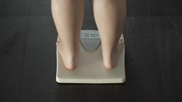 Female stepping on scales, word too much appearing on screen, overweight, rear