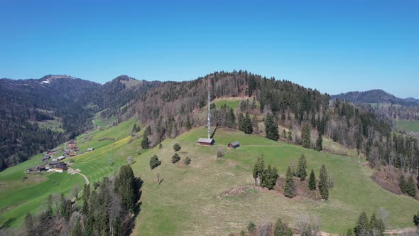 Aerial forward to a telecommunication tower on a rural hill in Switzerland.