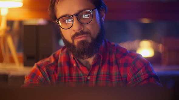 Portrait Of a Man Is Working On Laptop Computer With Glasses At Night. Close Up. Businessman Looking
